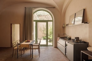 A compact kitchen with a dining area, a large arched window, and a view of greenery outside. - Serra Novecento Garden Suite & Residence _La Veranda_ (Bellano)
