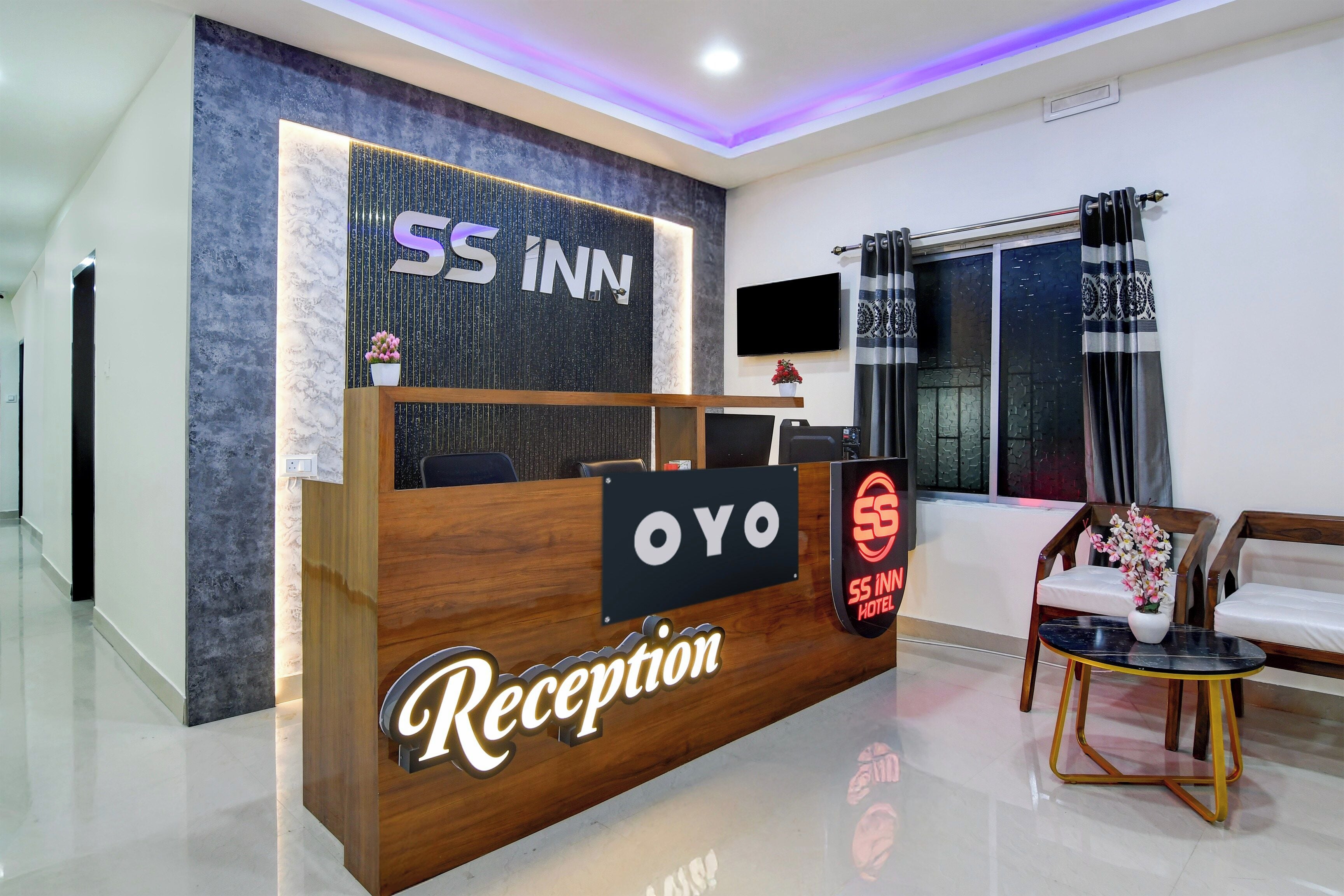Zona de recepción de un hotel, con mostrador, televisor y ventana con cortinas.