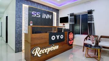 Zona de recepción de un hotel, con mostrador, televisor y ventana con cortinas.