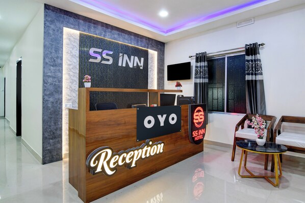 Zona de recepción de un hotel, con mostrador, televisor y ventana con cortinas.