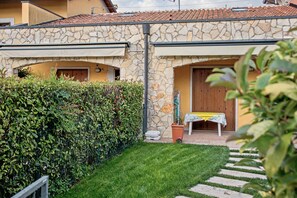 A stone building with a tiled roof, a small garden with a table and chairs, and a wooden door. - Apartment 'Casa Vacanze Da Ricky App 6' with Shared Pool, Wi-Fi and Air Conditioning (Peschiera del Garda)
