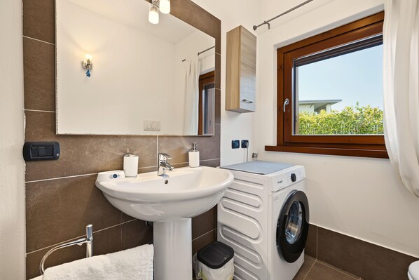 Un bagno moderno con lavandino, specchio, porta asciugamani e una finestra vista verde.