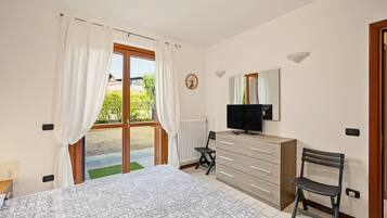 Een slaapkamer met een bed, een dressoir, een stoel, een televisie en een raam met gordijnen.
