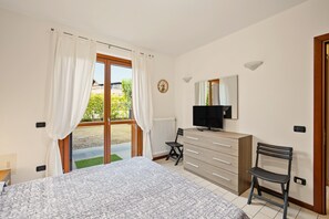 Una camera da letto con un letto, una cassettiera, una sedia, una televisione e una finestra con tende.
