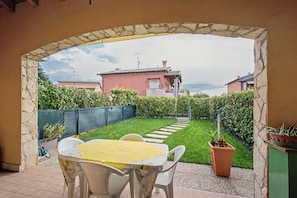 A patio with a table and chairs, a stone archway, a grassy lawn, and a building in the background. - Apartment 'Casa Vacanze Da Ricky App 6' with Shared Pool, Wi-Fi and Air Conditioning (Peschiera del Garda)