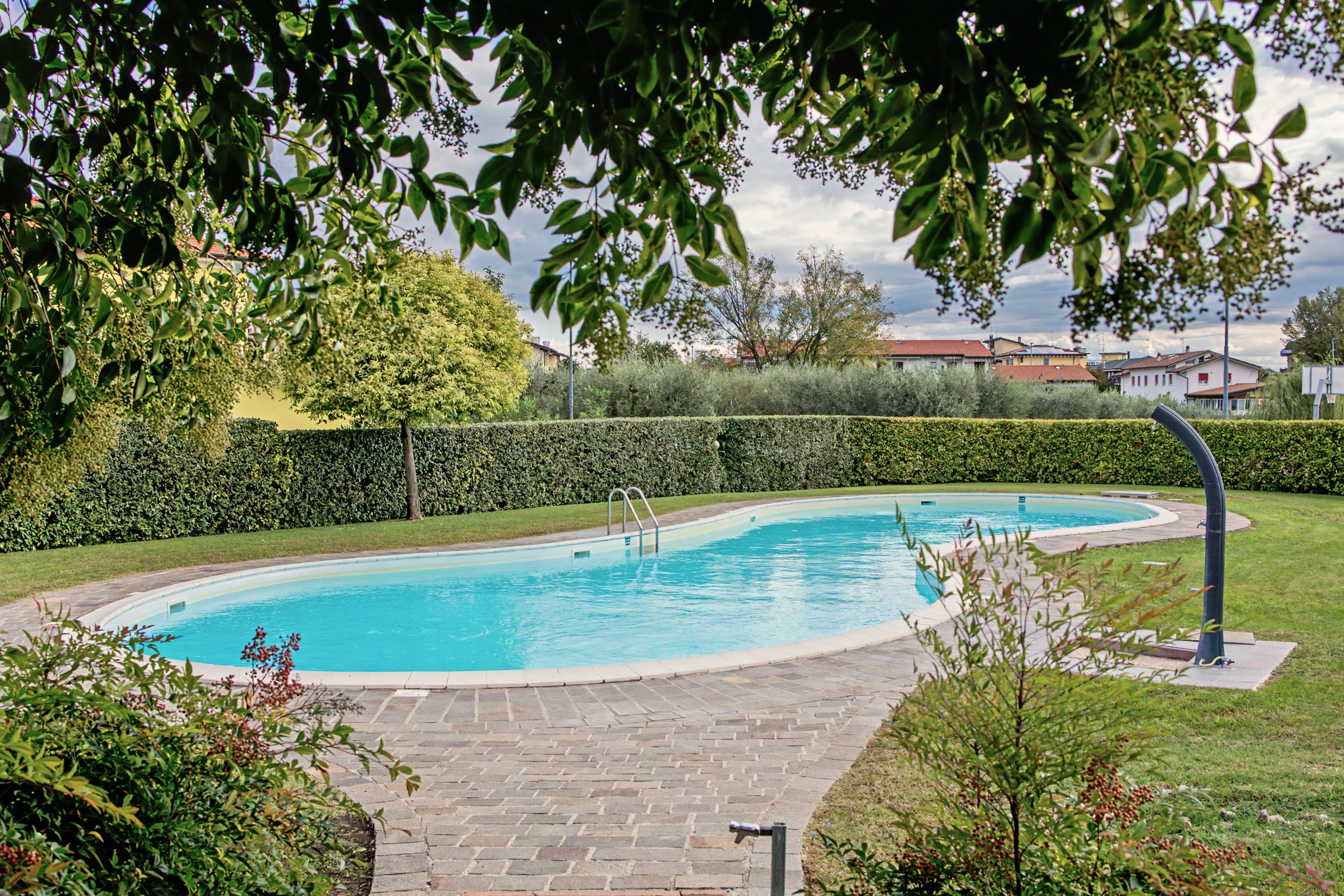 Une piscine bordée d’une allée dallée, entourée de haies et d’arbres bien entretenus.