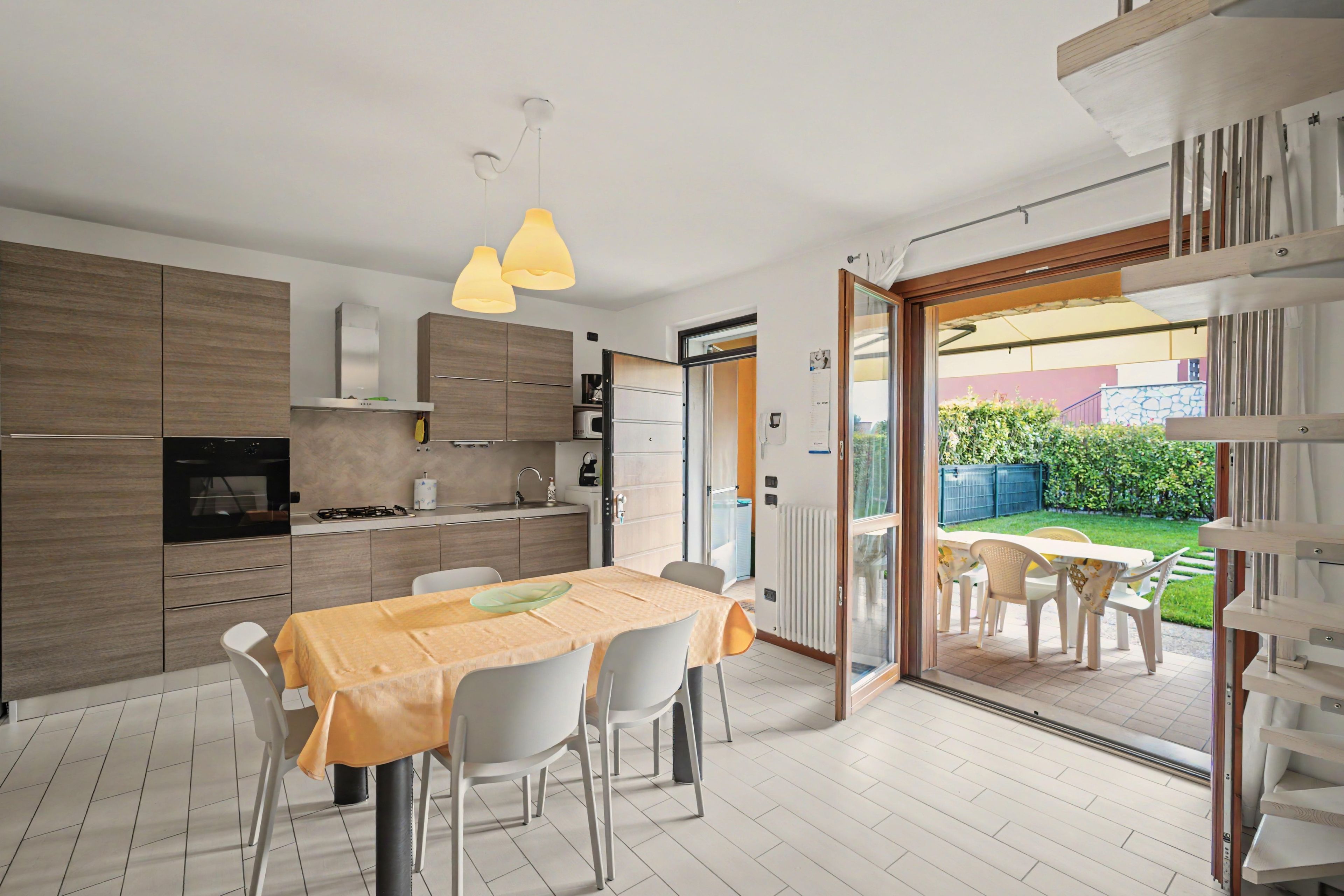 A modern kitchen with a dining area, a view of the garden, and a sliding glass door leading outside.