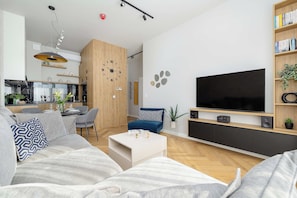 A modern living room with a large flat-screen TV, a sofa, a coffee table, and a dining area with a kitchen in the background. - Mrzezyno | Nadmorska 7F | Comfortable Apartment | Air conditioning | Parking (Mrzeżyno)