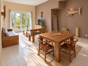 A spacious living area with a wooden dining table, chairs, a sofa, and a television. - Bazaar Square Lodges - Jasmin (Grand Baie)