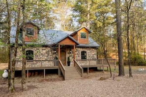 A cabin with a stone facade, wooden deck, and a porch with a staircase. - Game Console-Horseshoe Pit-Swing Chairs-Hot Tub-Hearthstone (Broken Bow)