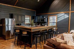 A modern kitchen with a central island, bar stools, and a refrigerator. - Game Console-Horseshoe Pit-Swing Chairs-Hot Tub-Hearthstone (Broken Bow)