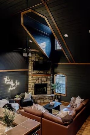 Ein gemütliches Wohnzimmer mit Kamin aus Stein, einer Ledersofa und einer Neonreklame.