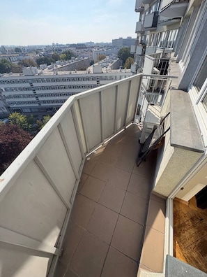Ein schmaler Balkon mit Blick auf eine Stadtlandschaft, mit Fliesenboden und Metallgeländer.