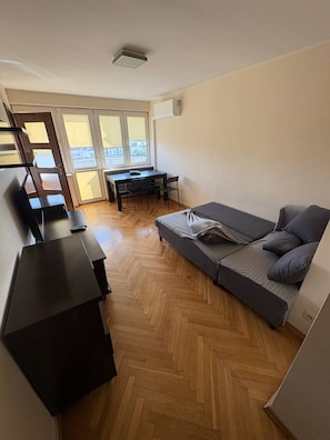 Ein gemütliches Zimmer mit einer Sitzecke, einem Schreibtisch und einem Stuhl. Ein Fenster lässt Tageslicht herein und bietet einen Blick nach draußen.