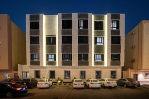 A multi-story hotel with a modern facade, multiple balconies, and a parking area with several cars. - Luxury 1BR  Self Entry Near
KAFD Riyadh Blvd (Riyadh)