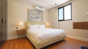 A hotel room with a bed, two bedside lamps, a large abstract painting, an air conditioning unit, a window with curtains, and a wooden floor. - Luxury 1BR  Self Entry Near
KAFD Riyadh Blvd (Riyadh)
