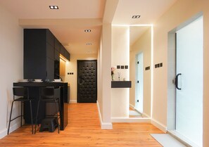 A modern kitchen with black cabinets, a bar area with stools, and a wooden floor. - Luxury 1BR  Self Entry Near
KAFD Riyadh Blvd (Riyadh)
