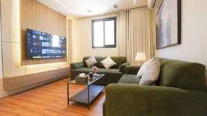 A modern living room with a flat-screen TV, two green sofas, a coffee table, and a window with curtains. - Luxury 1BR  Self Entry Near
KAFD Riyadh Blvd (Riyadh)