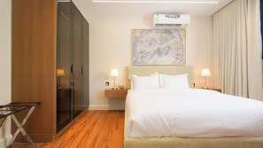 A hotel room with a bed, bedside lamps, a nightstand, a painting, an air conditioning unit, and a wooden wardrobe. - Luxury 1BR  Self Entry Near
KAFD Riyadh Blvd (Riyadh)