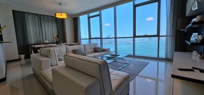 A modern living room with a large window, a sofa set, and a dining area. - Amazing Full Sea View High floor apartment 3bedrooms 4bathrooms.5star facilities (Manama)