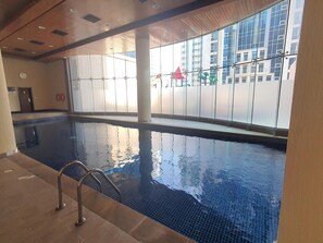 An indoor swimming pool with clear glass walls, a tiled floor, and a metal ladder. - Amazing Full Sea View High floor apartment 3bedrooms 4bathrooms.5star facilities (Manama)