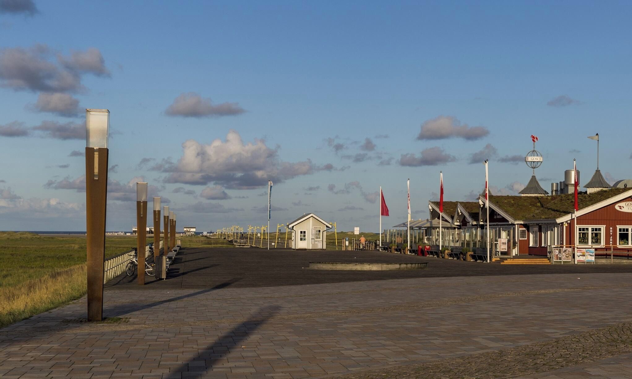 Une promenade en bord de mer avec un petit bâtiment, des drapeaux et un restaurant.