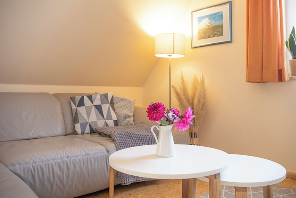 Un salon chaleureux avec un canapé, une petite table, une lampe et un vase rempli de fleurs.