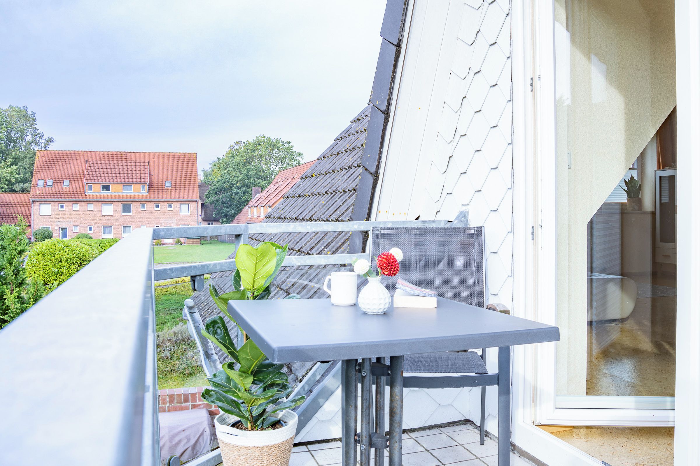 Ein Balkon mit Tisch, Blumentöpfen und Blick auf ein Gebäude mit rotem Dach.