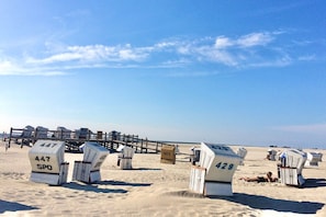 Des chaises de plage numérotées, une jetée en bois et un ciel dégagé.