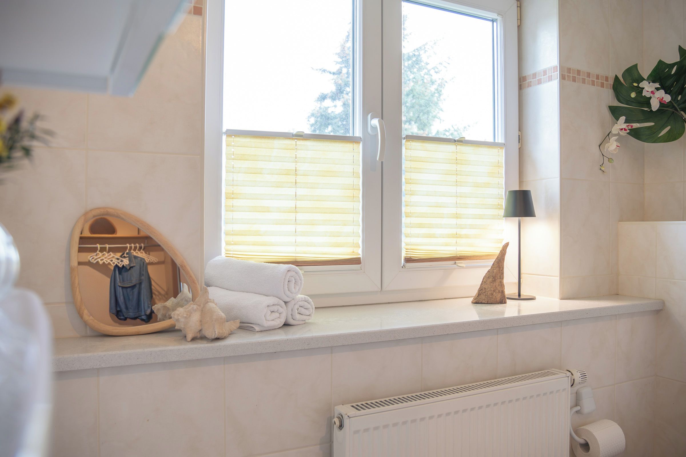 Ein Badezimmer mit Fenster, Handtuchhalter, Spiegel, Lampe und Heizkörper.