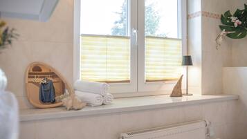 Ein Badezimmer mit Fenster, Handtuchhalter, Spiegel, Lampe und Heizkörper.