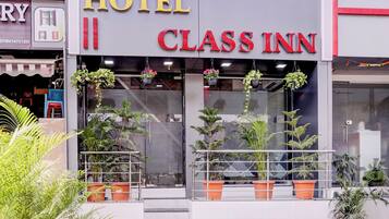 A hotel named 'CLASS INN' with a modern facade, large windows, and potted plants at the entrance.