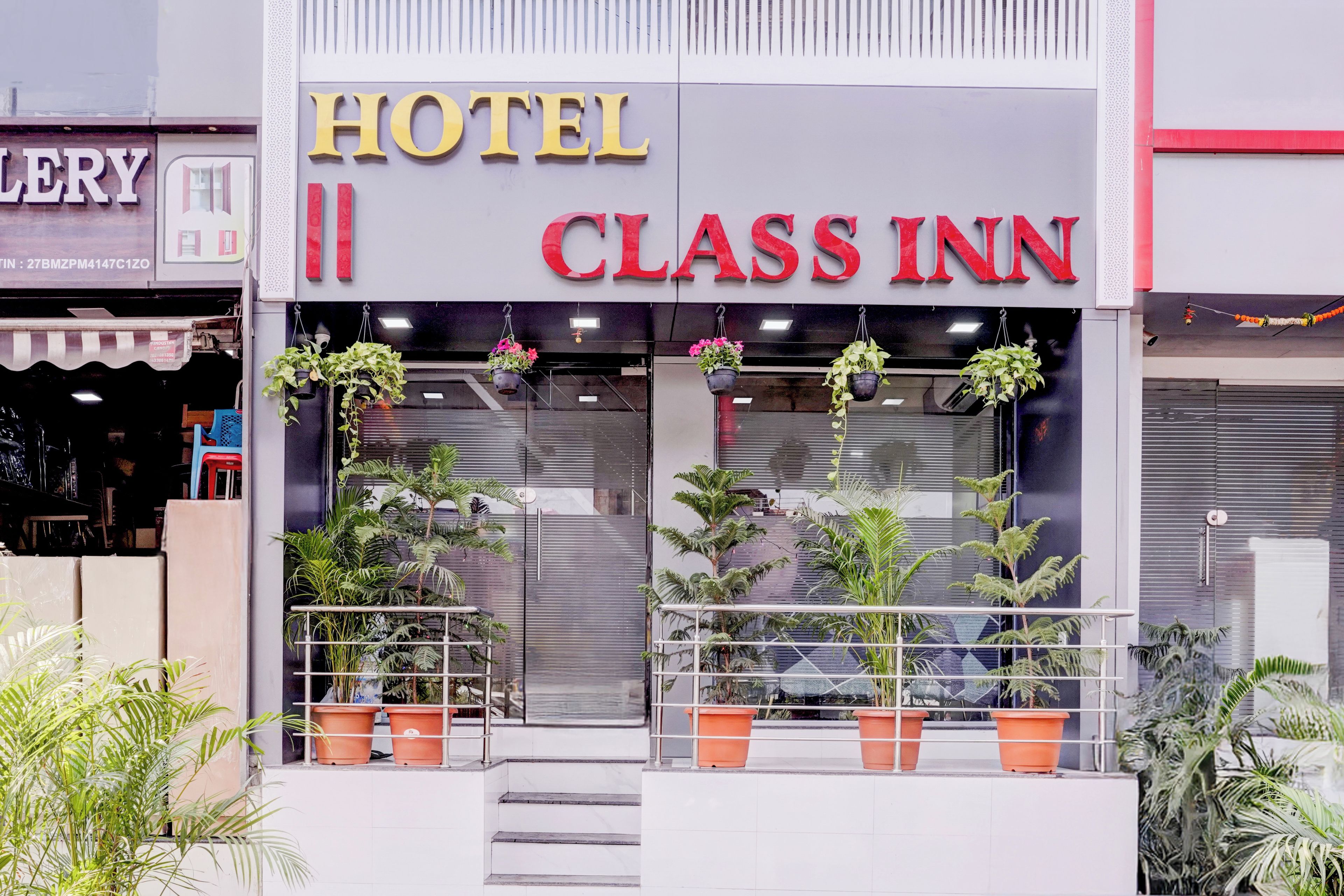A hotel named 'CLASS INN' with a modern facade, large windows, and potted plants at the entrance.