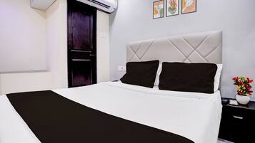 A hotel room with a bed, a nightstand, a vase with flowers, and a wall with three framed pictures.