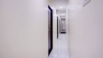 A corridor with white walls and a marble floor leading to a door at the end.