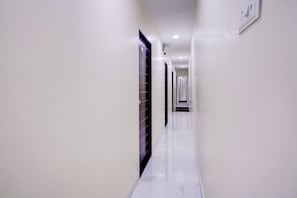 A corridor with white walls and a marble floor leading to a door at the end. - Hotel O Class Inn (Mumbai)