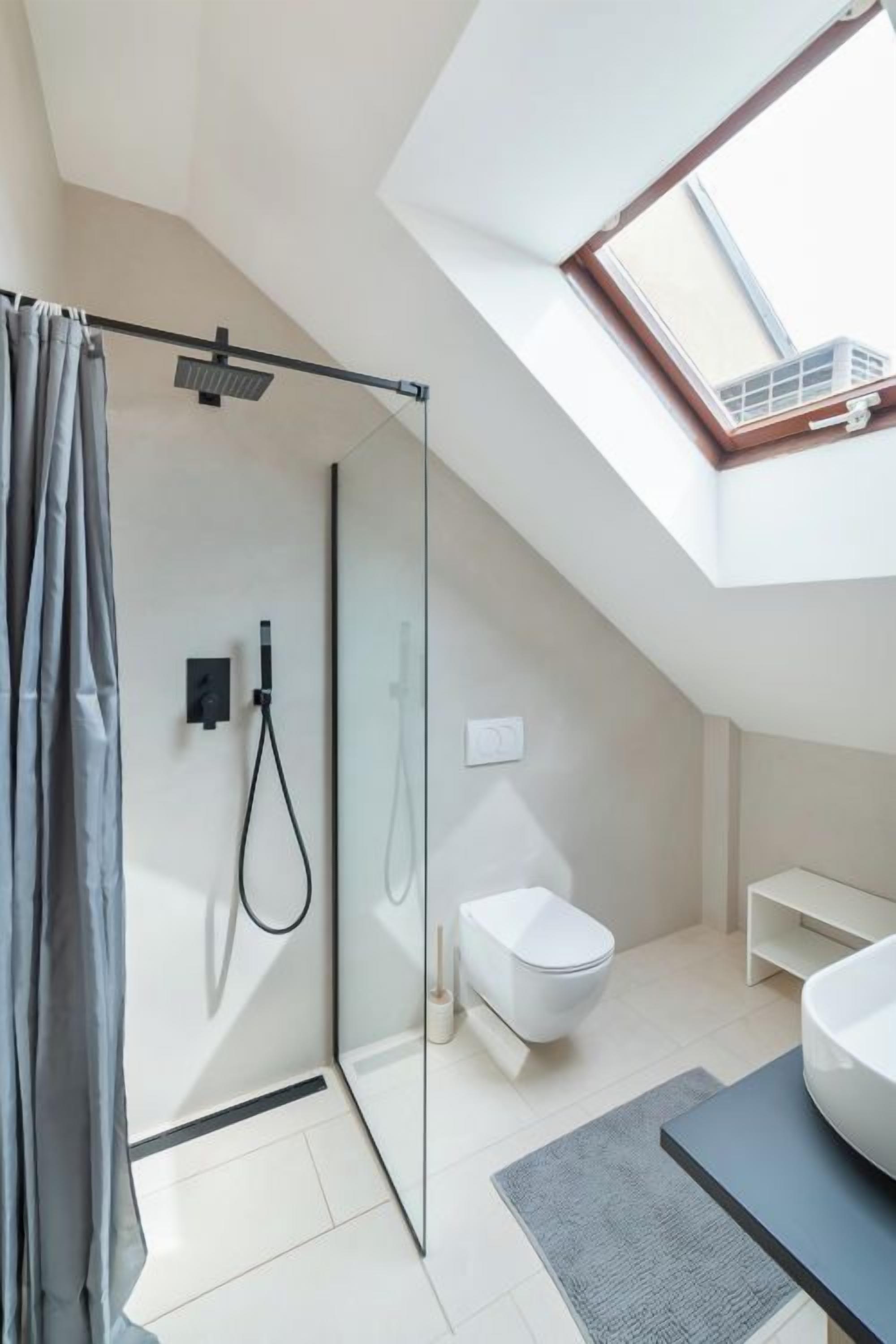 Ein modernes Badezimmer mit Duschkabine aus Glas, Toilette und einem großen Oberlicht.