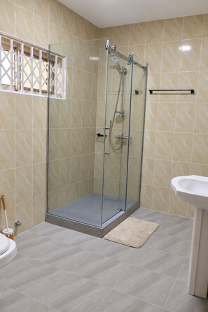 Een moderne badkamer met een douchecabine van glas, een witte wastafel en een vloer van beige tegels.