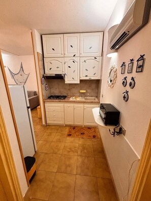 Cocina compacta con muebles blancos, estufa a gas y una pequeña encimera.
