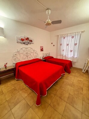 Un dormitorio con dos camas, un ventilador de techo, una ventana con cortinas y una pared con detalles decorativos.