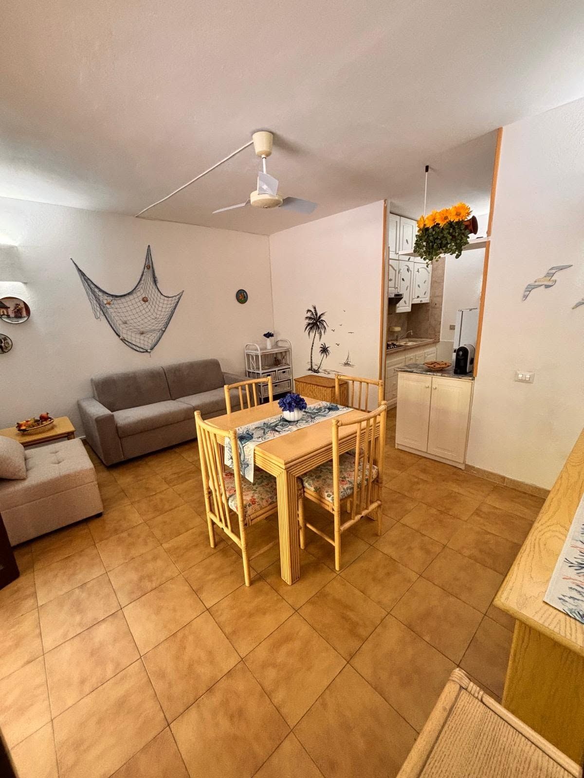 A compact living space with a dining area, a sofa, a ceiling fan, and a kitchen area.