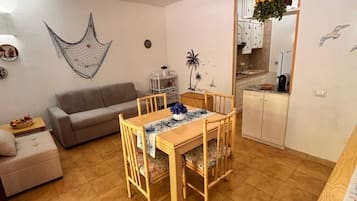 A compact living space with a dining area, a sofa, a ceiling fan, and a kitchen area.