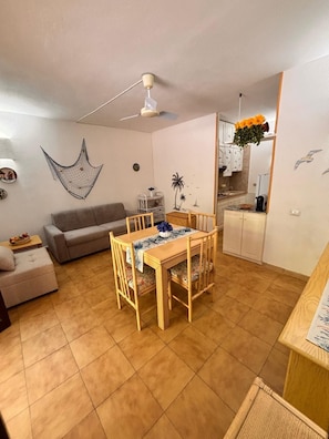 En kompakt opholdsstue med spiseplads, en sofa, loftventilator og et tekøkken.