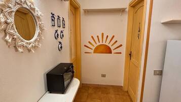 A hallway with a macrame wall decoration, a wall-mounted air conditioner, a wall art of a sun, and a trash bin.