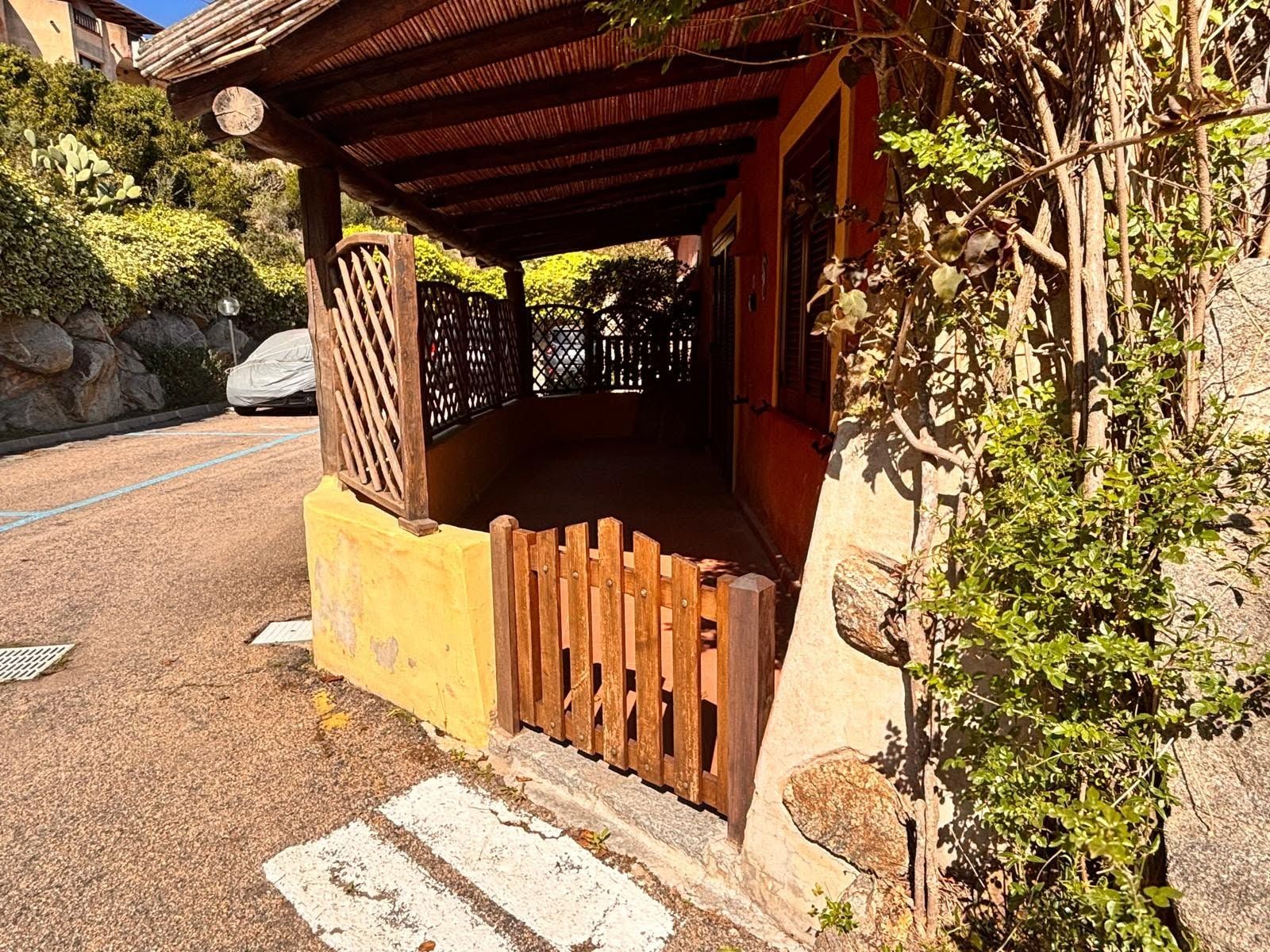 A covered porch with a wooden fence, a stone wall, and a vehicle parked in the background.