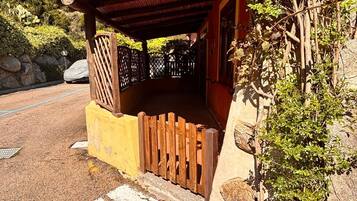 A covered porch with a wooden fence, a stone wall, and a vehicle parked in the background.