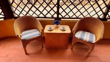 A balcony with two wicker chairs, a small table with two cups, and a decorative vase.