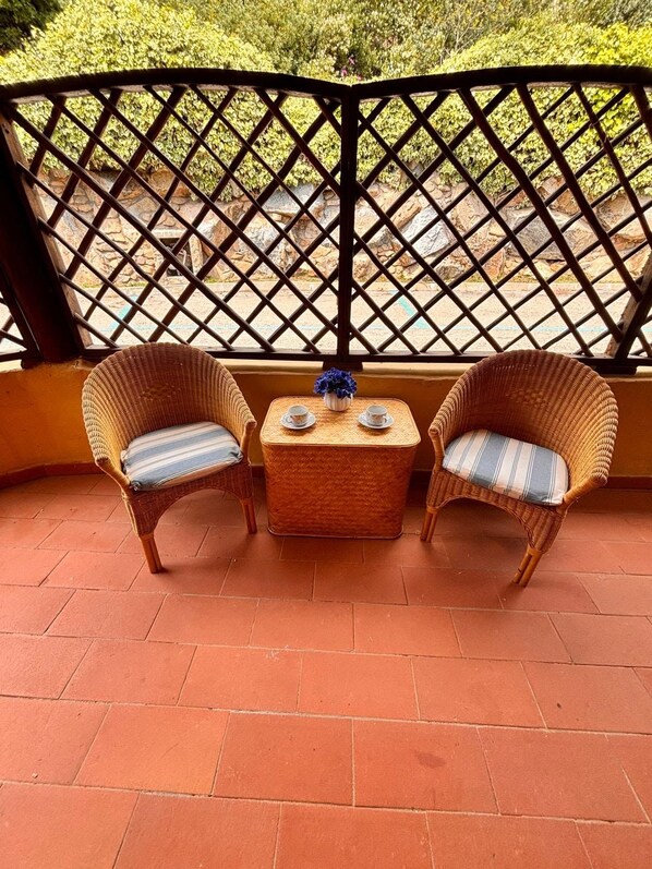 Un balcón con dos sillones de mimbre, una mesita con dos tazas y un jarrón decorativo.