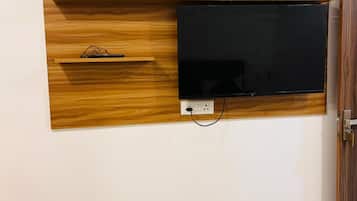Un téléviseur fixé au mur, avec un panneau en bois et un vase rempli de fleurs rouges.