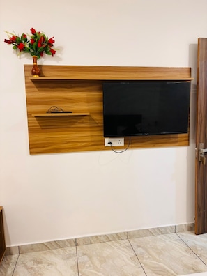 A wall-mounted TV with wooden paneling and a vase of red flowers. - Raj Rani Complex And Hotel Restaurant (Mainpuri)